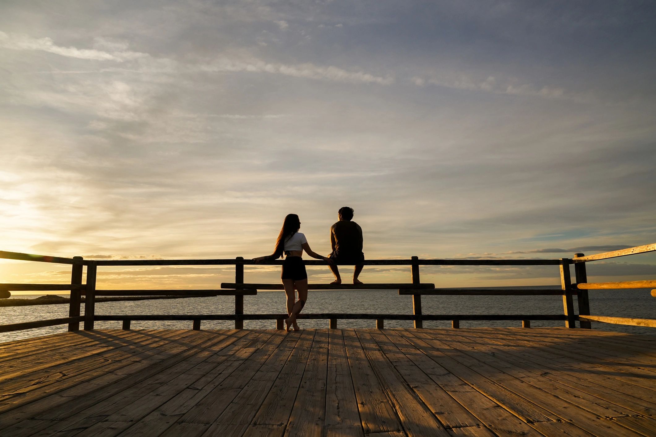 Couple holding hands watching sunset from a pier